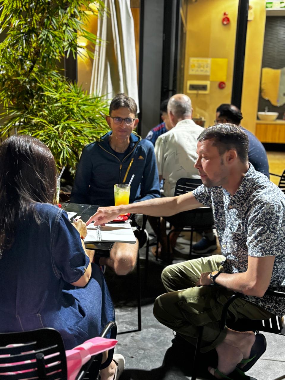 Three members using notes during a focused table conversation at the Friday, April 24, 2026 language exchange.